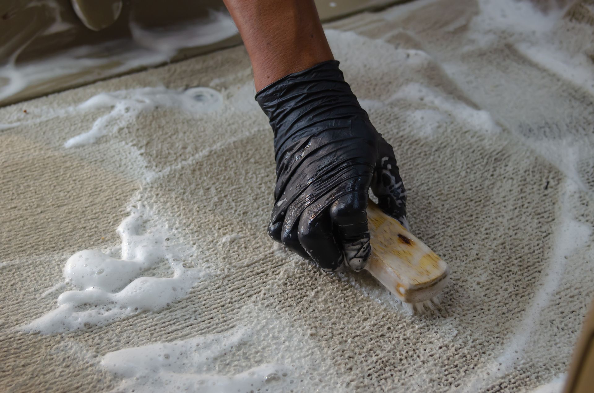 Main gantée utilisant un pinceau pour étaler de la mousse blanche sur une moquette.