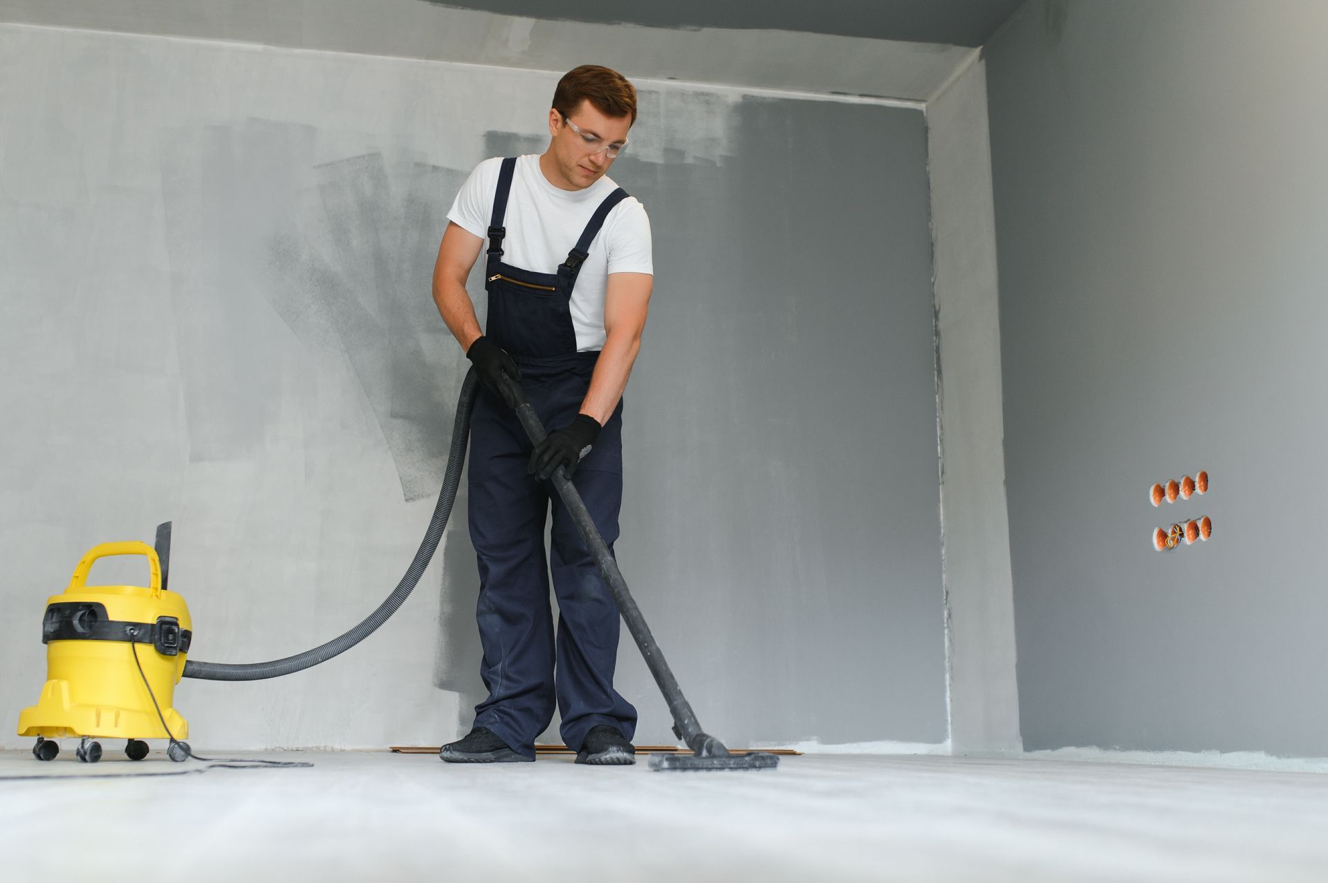 Un agent du nettoyage utilise un aspirateur dans une pièce en rénovation.