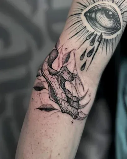 Tatuaje de una garra y un ojo con lágrimas en el brazo. Blanco y negro, detallado.