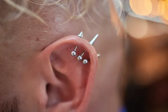 Primer plano de una oreja con múltiples perforaciones, incluidos tres pendientes de plata y un gran pendiente con púas.