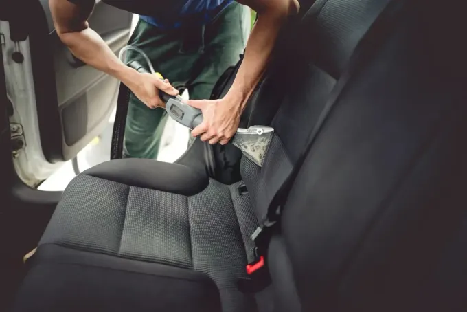 Persona abrochándose el cinturón de seguridad en un coche; asiento negro, puerta del coche abierta.