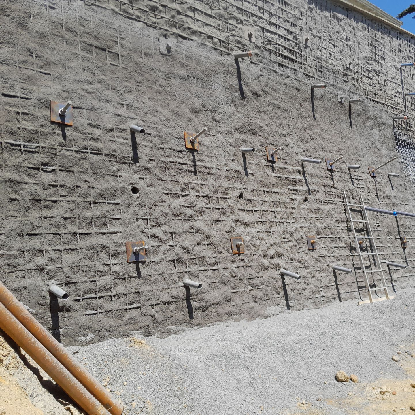 Mur de soutènement en pierre avec ancrages de barres d'armature apparents et une échelle sur un chantier de construction en gravier