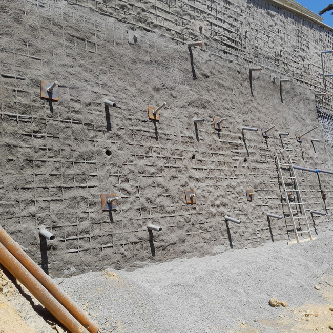 Mur de soutènement en pierre avec ancrages apparents et gravier à la base, vu sur un chantier de construction