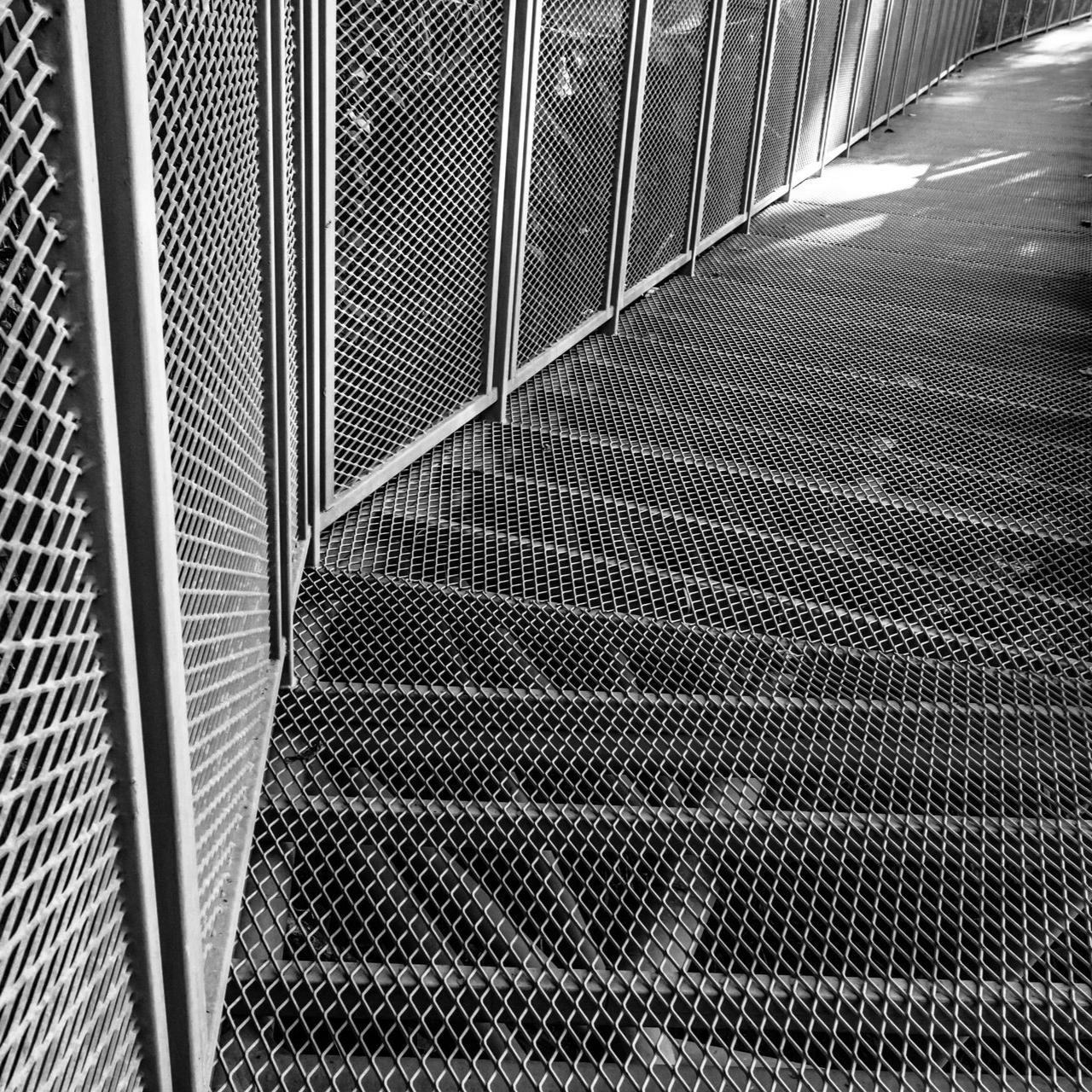 Vue en noir et blanc d'une passerelle métallique grillagée