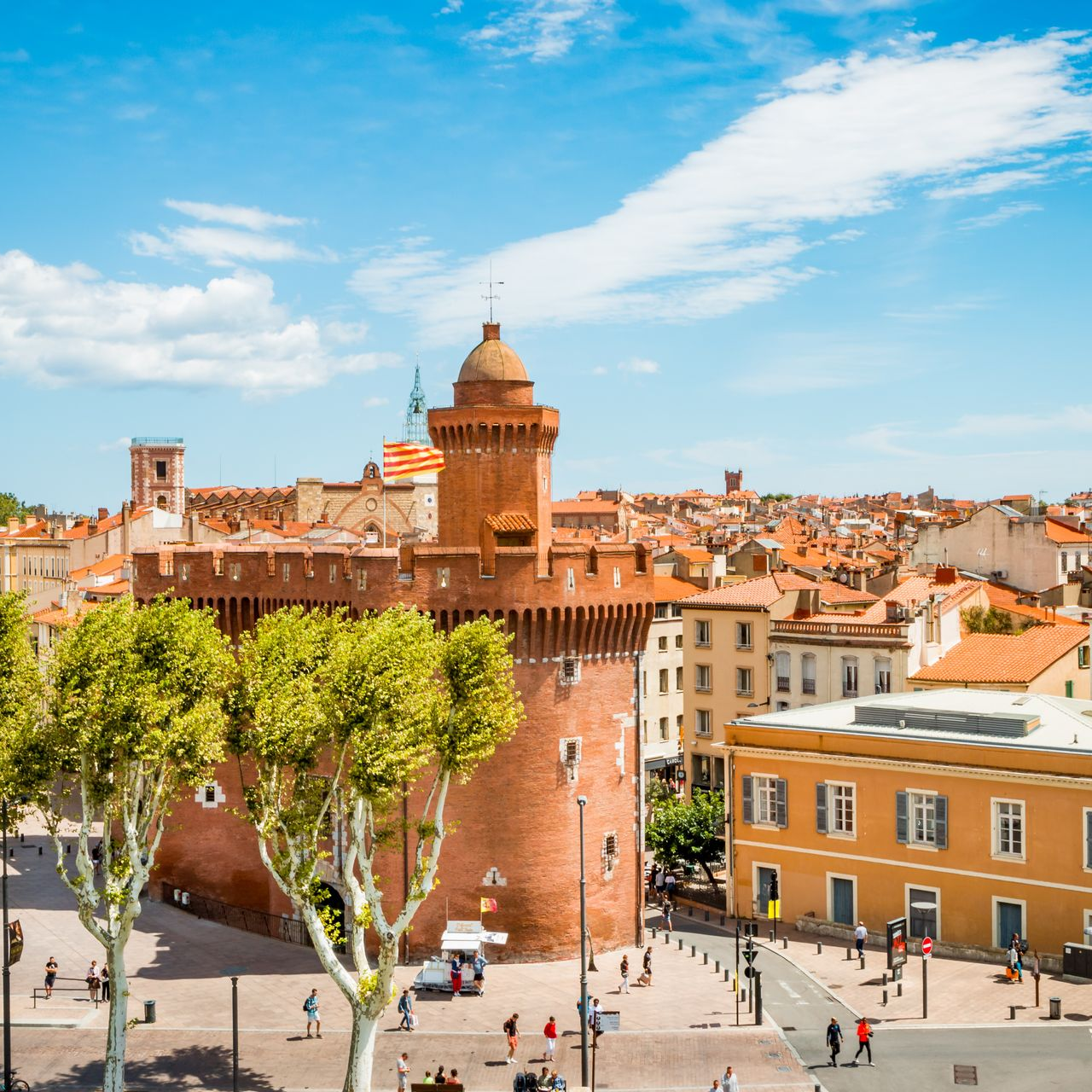 Tour historique en briques rouges et place de la ville sous un ciel d'un bleu éclatant, avec des bâtiments et des arbres à proximité