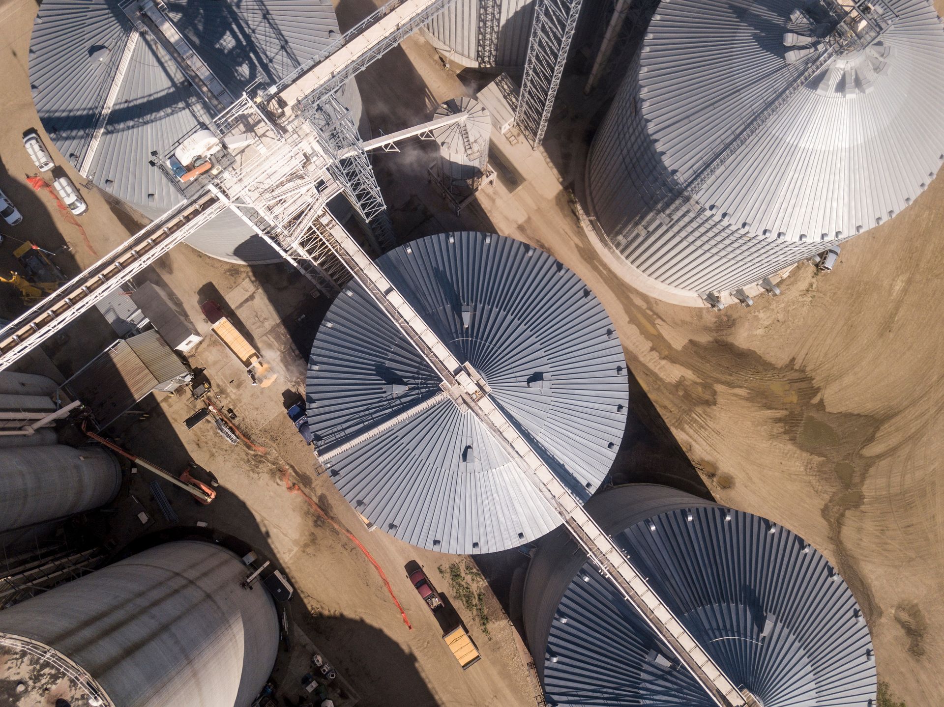 Vue aérienne de grands silos à grains d'argent dans une zone de stockage industrielle avec des chemins de terre