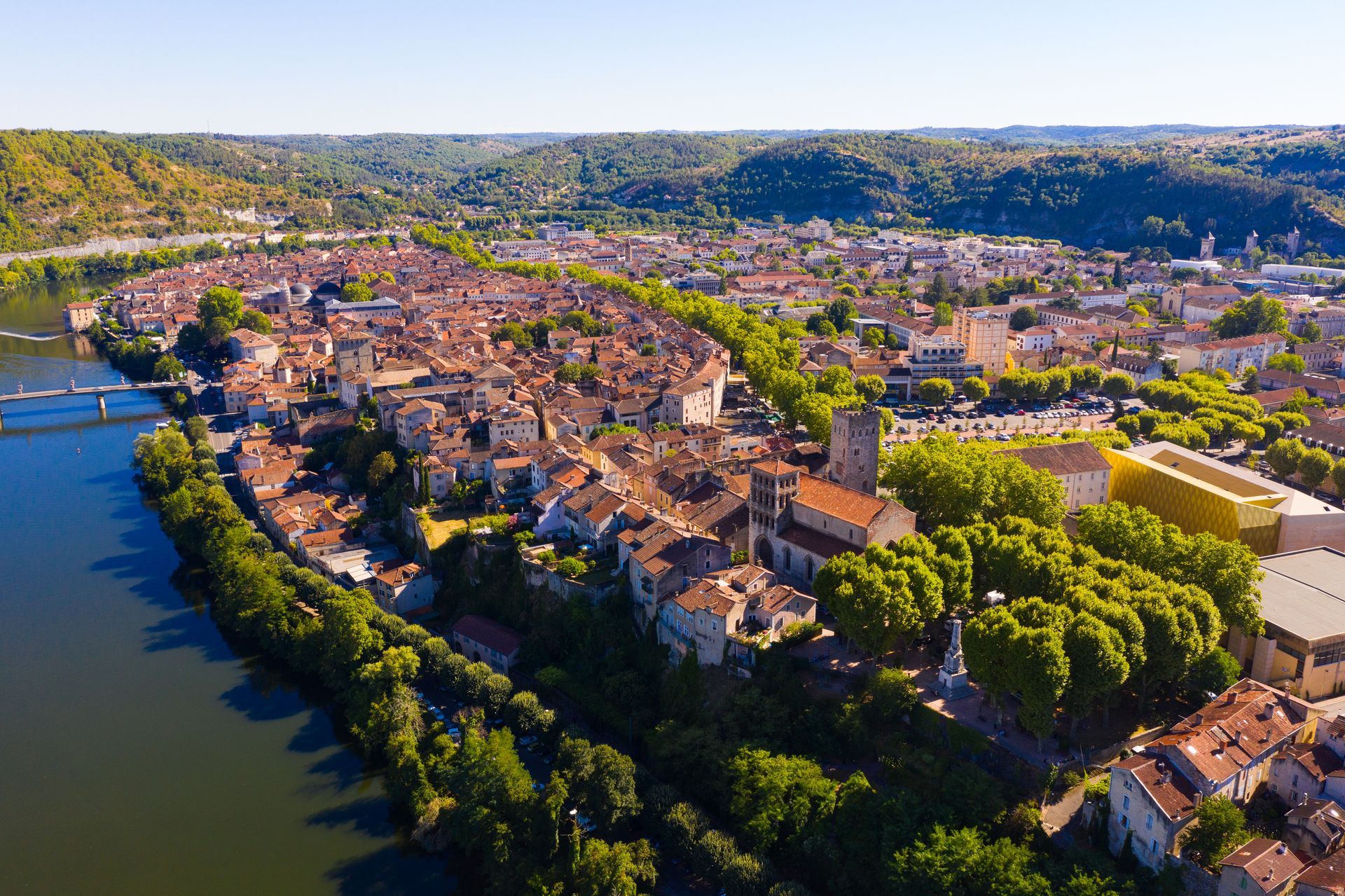 Vue aérienne d'une ville aux toits de tuiles rouges et aux collines verdoyantes, avec un fleuve à côté