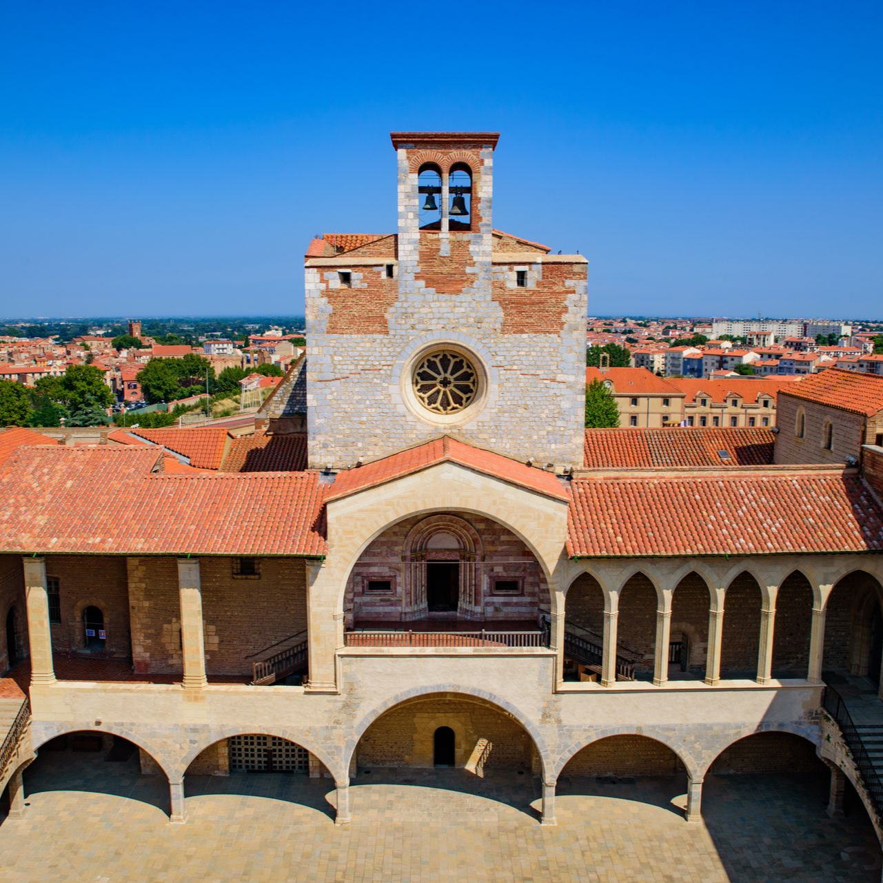 Cour historique avec des arches en pierre et une tour centrale sous un ciel d'un bleu éclatant