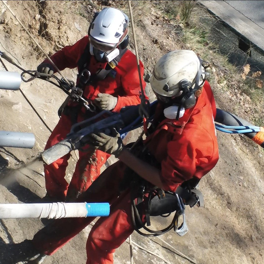 Deux alpinistes en tenue rouge et casques descendent en rappel une falaise rocheuse, en tenant des cordes