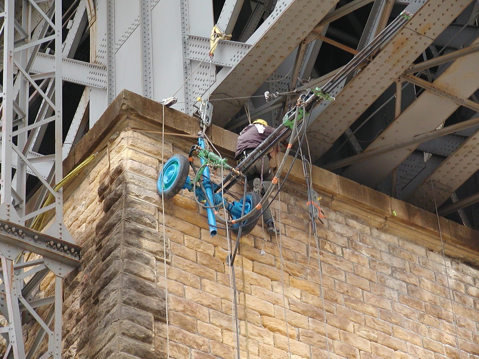 Ouvrier portant un harnais de sécurité réparant un mur de pierre sous un pont