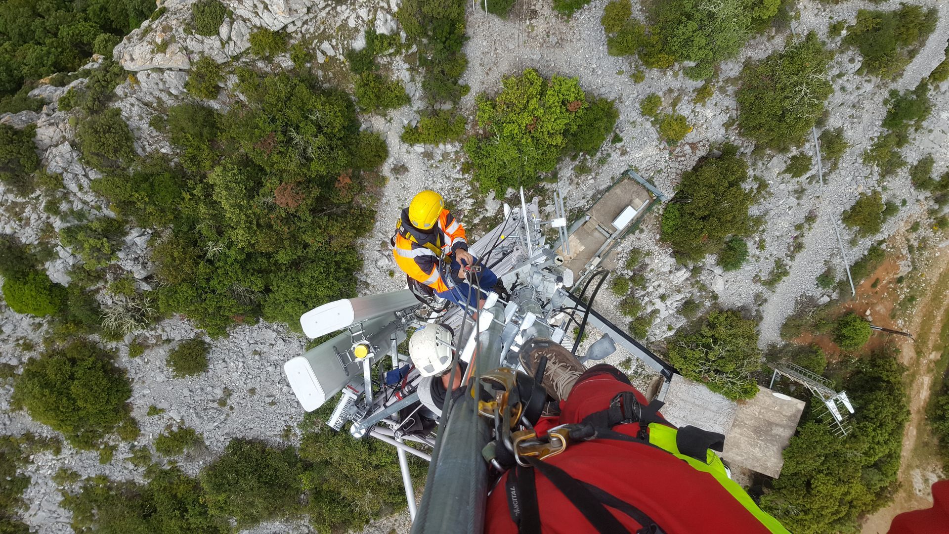 Ouvriers portant des casques sur une antenne métallique, vu d'en haut, avec équipement de travaux en hauteur