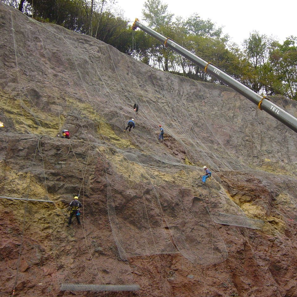 Des ouvriers descendent en rappel une falaise rocheuse abrupte et posent un grillage de protection