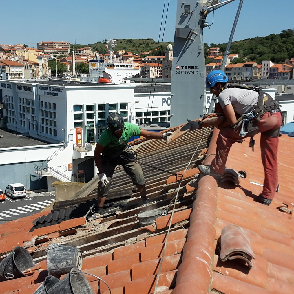 Deux ouvriers en tenue de sécurité réparent un toit en tuiles de terre cuite sur un bâtiment