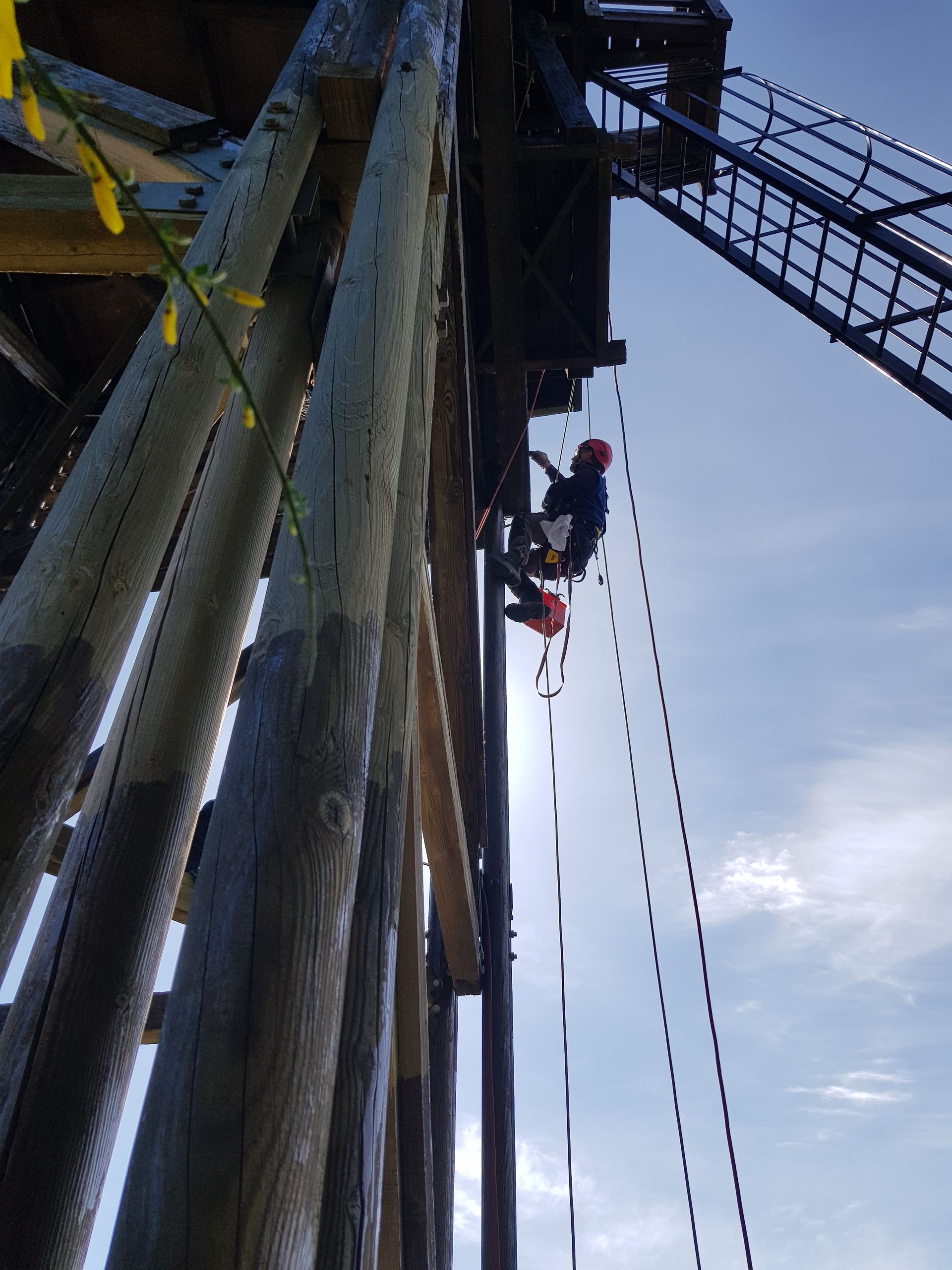 Ouvrier suspendu par des cordes à une haute structure, sous un ciel nuageux