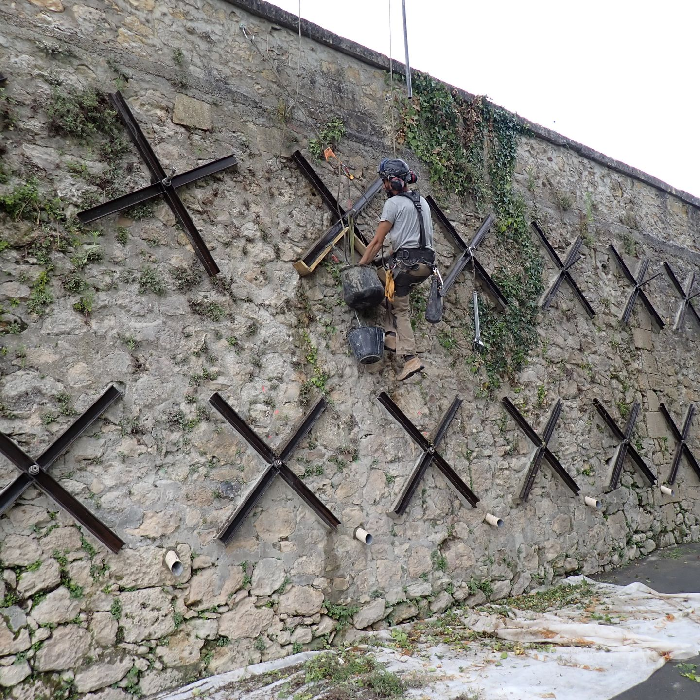 Un ouvrier utilise un marteau sur un mur de pierre renforcé par de grandes étais noires en forme de X