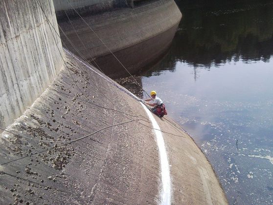Ouvrier travaillant sur corde sur un ouvrage bétonné près d'un cours d'eau