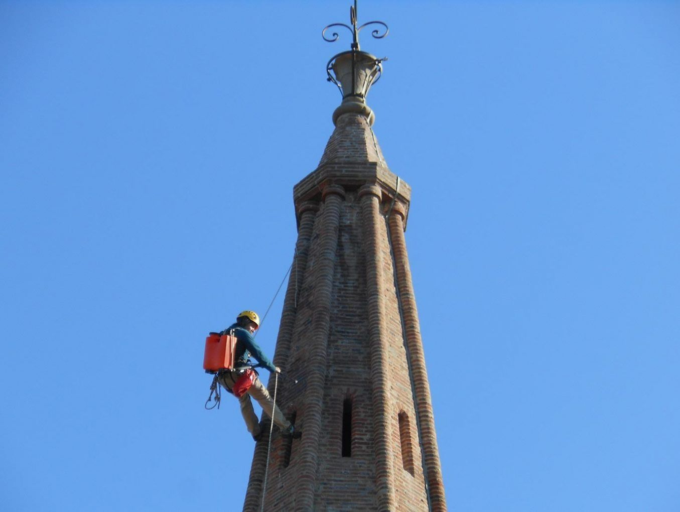 Ouvrier réalisant des travaux sur corde au niveau du clocher d'un monument ancien