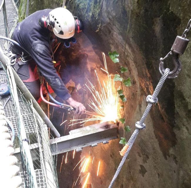 Un ouvrier soude sur une armature métallique dans une tranchée rocailleuse, des étincelles jaillissent