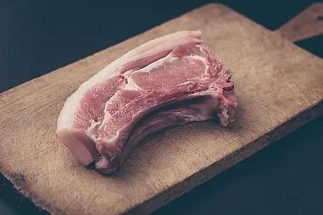 Un trozo de carne cruda reposa sobre una tabla de cortar de madera.