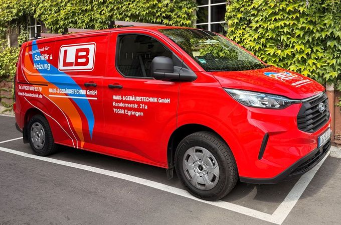 Ein roter Lieferwagen der Marke LB parkt auf einer Straße neben einem mit Efeu bewachsenen Gebäude.