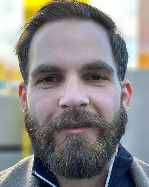 Ein Mann mit Brille und einem Band um den Hals blickt in die Kamera.