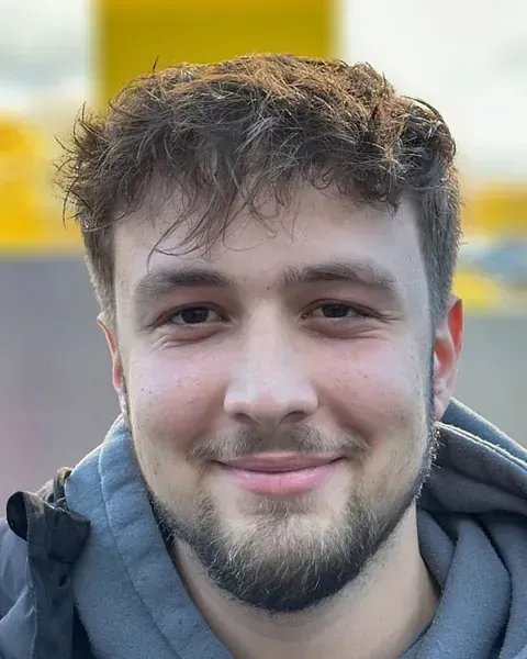 Ein junger Mann mit Bart lächelt in die Kamera.