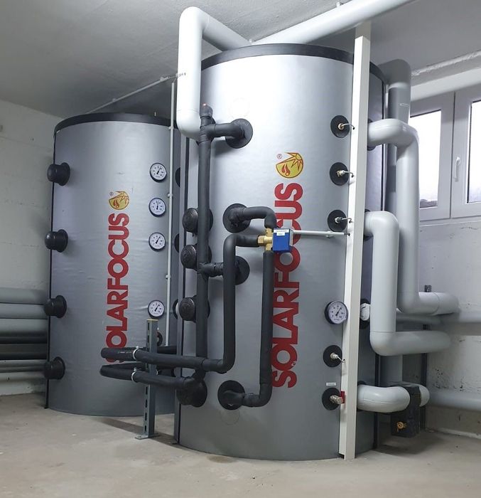 Industrielle Wassertanks und -leitungen in einem Hauswirtschaftsraum, gekennzeichnet mit „SOLARPLUS“, mit weißen Rohren und grauen Tanks.