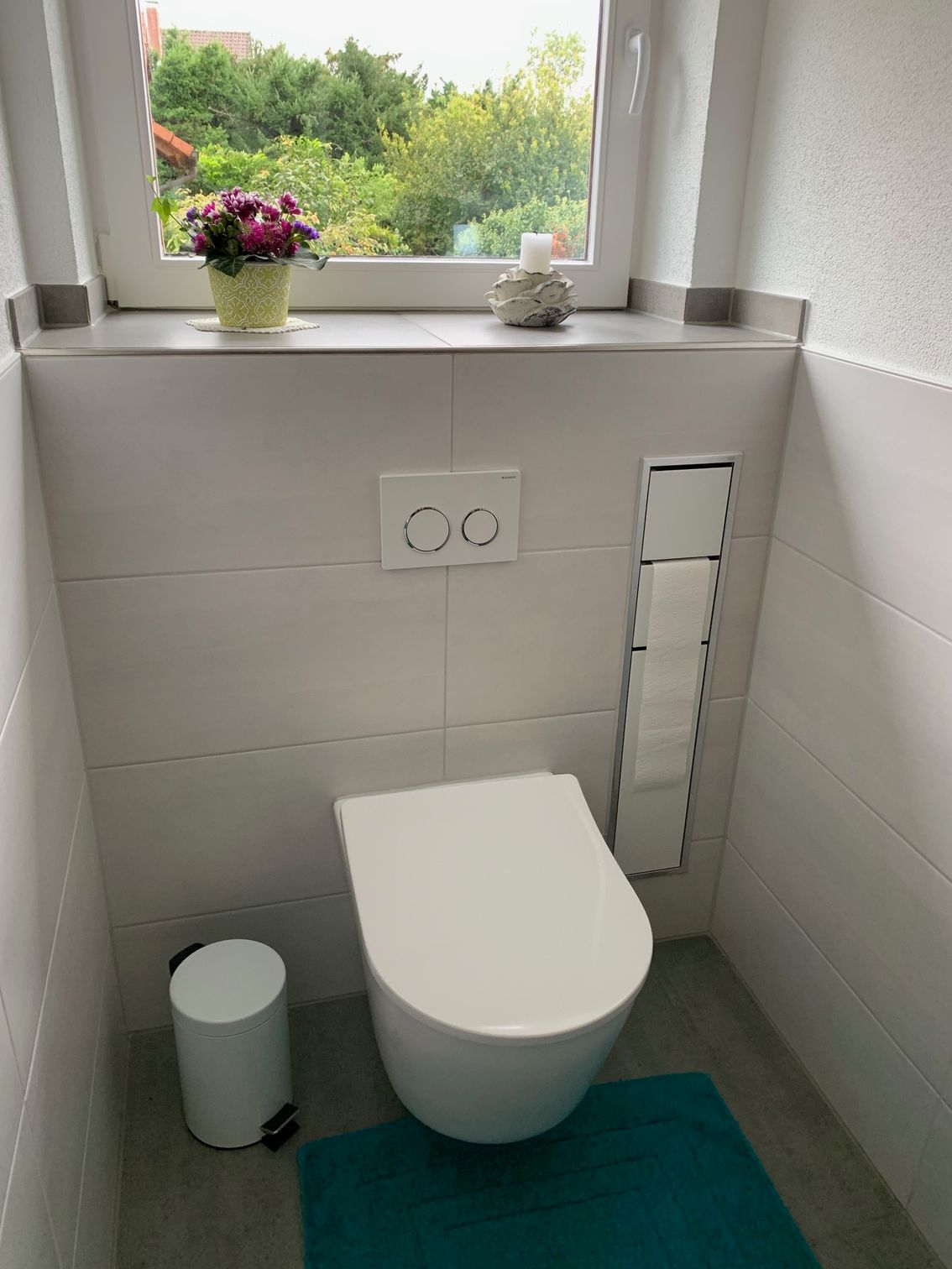 Eine weiße Toilette steht in einem Badezimmer neben einem Fenster.