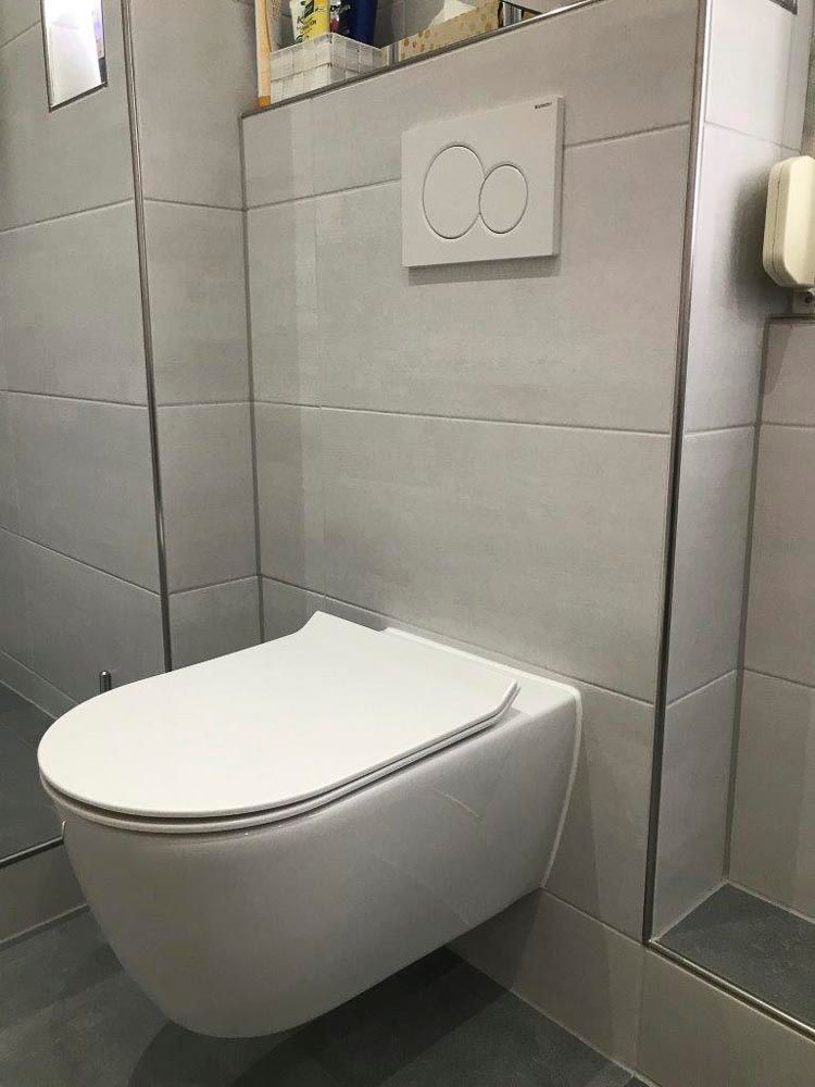 Eine weiße Toilette hängt neben einem Spiegel an der Wand in einem Badezimmer.
