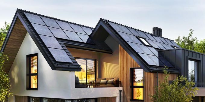 Modernes Haus mit weißen Wänden, dunklem Dach, warm beleuchteten Fenstern und einem Balkon in der Abenddämmerung.
