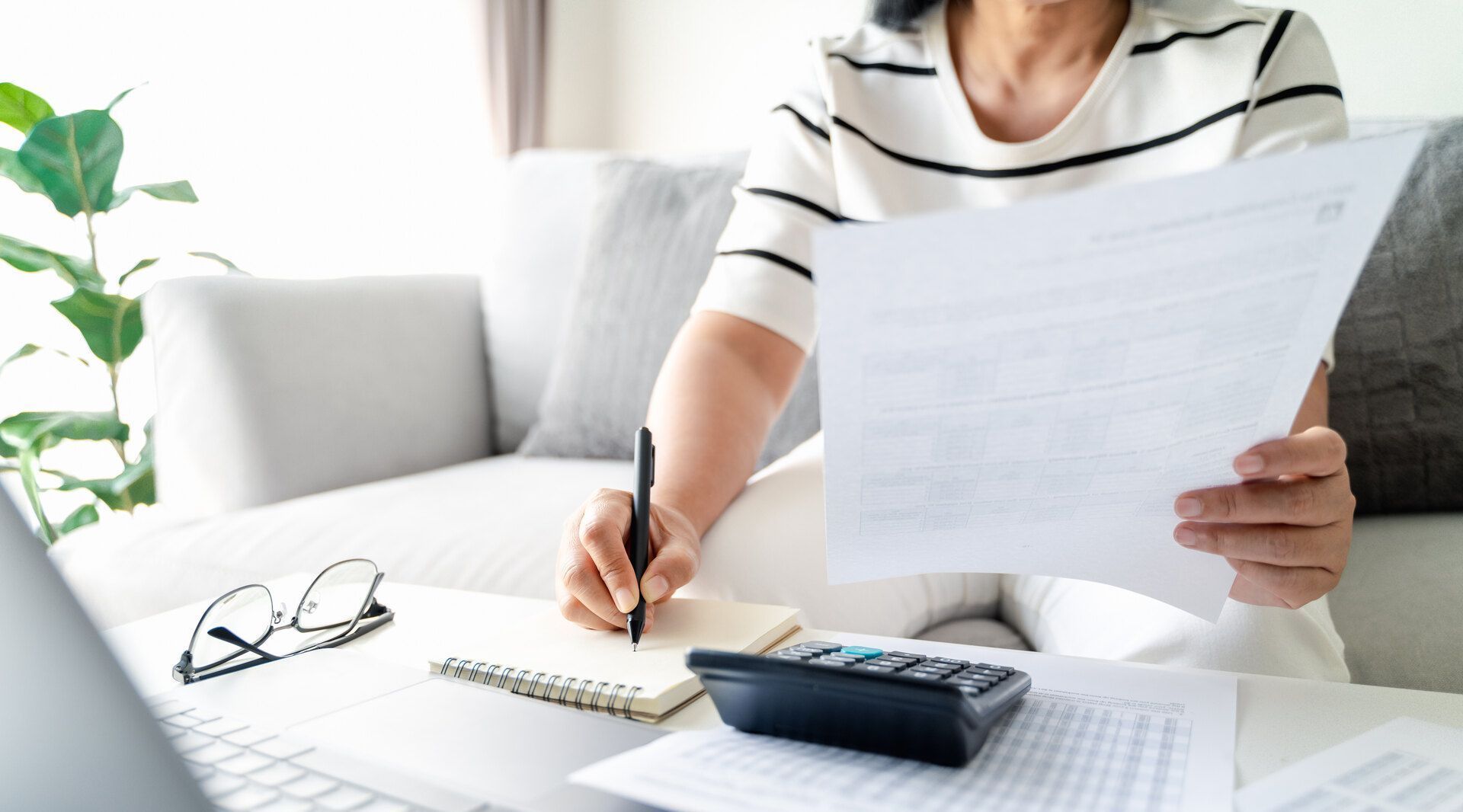 Eine Frau sitzt auf einer Couch und hält ein Stück Papier und einen Stift in der Hand.