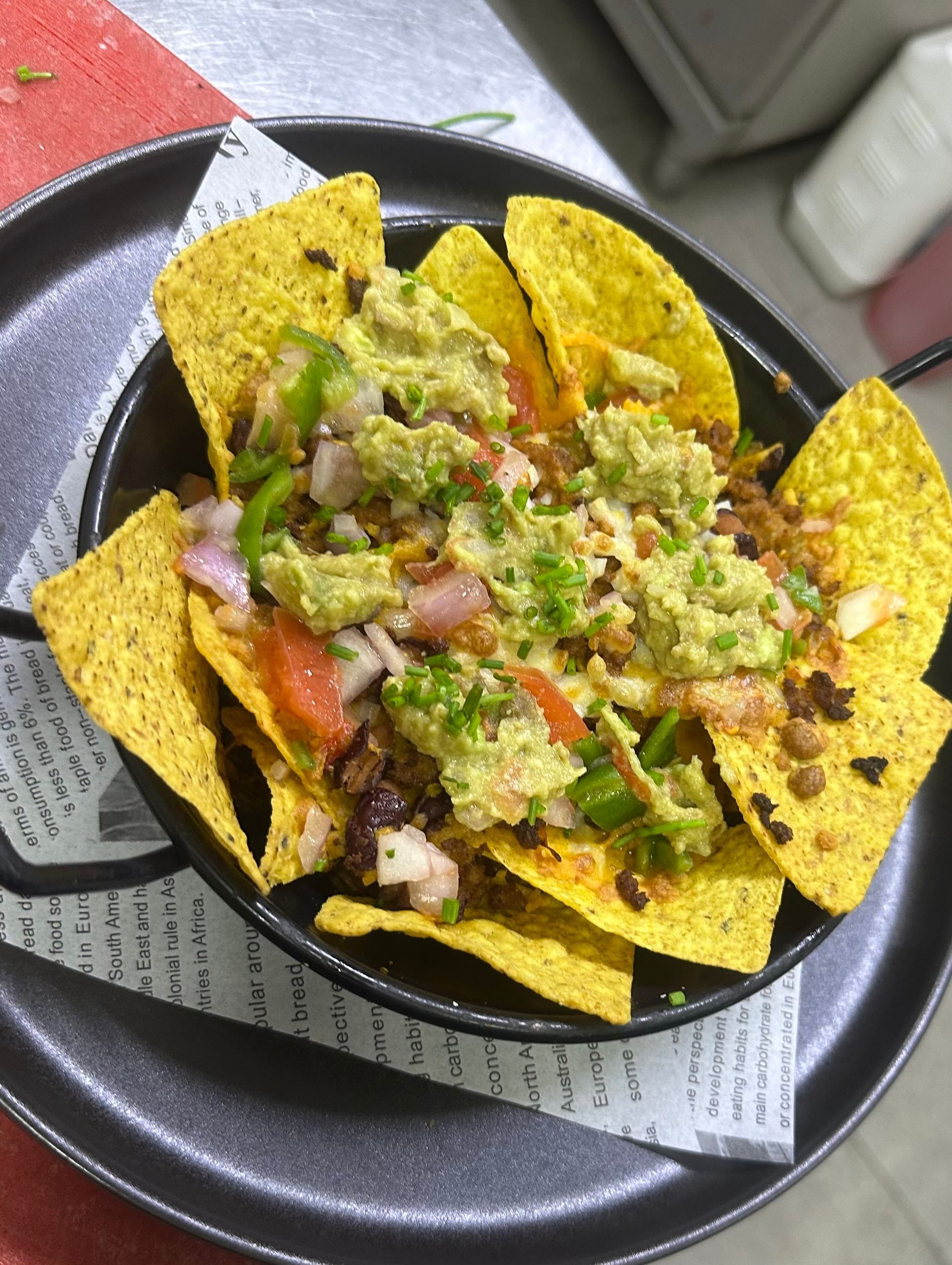 Nachos en bowl negro con guacamole, verduras y patatas fritas.