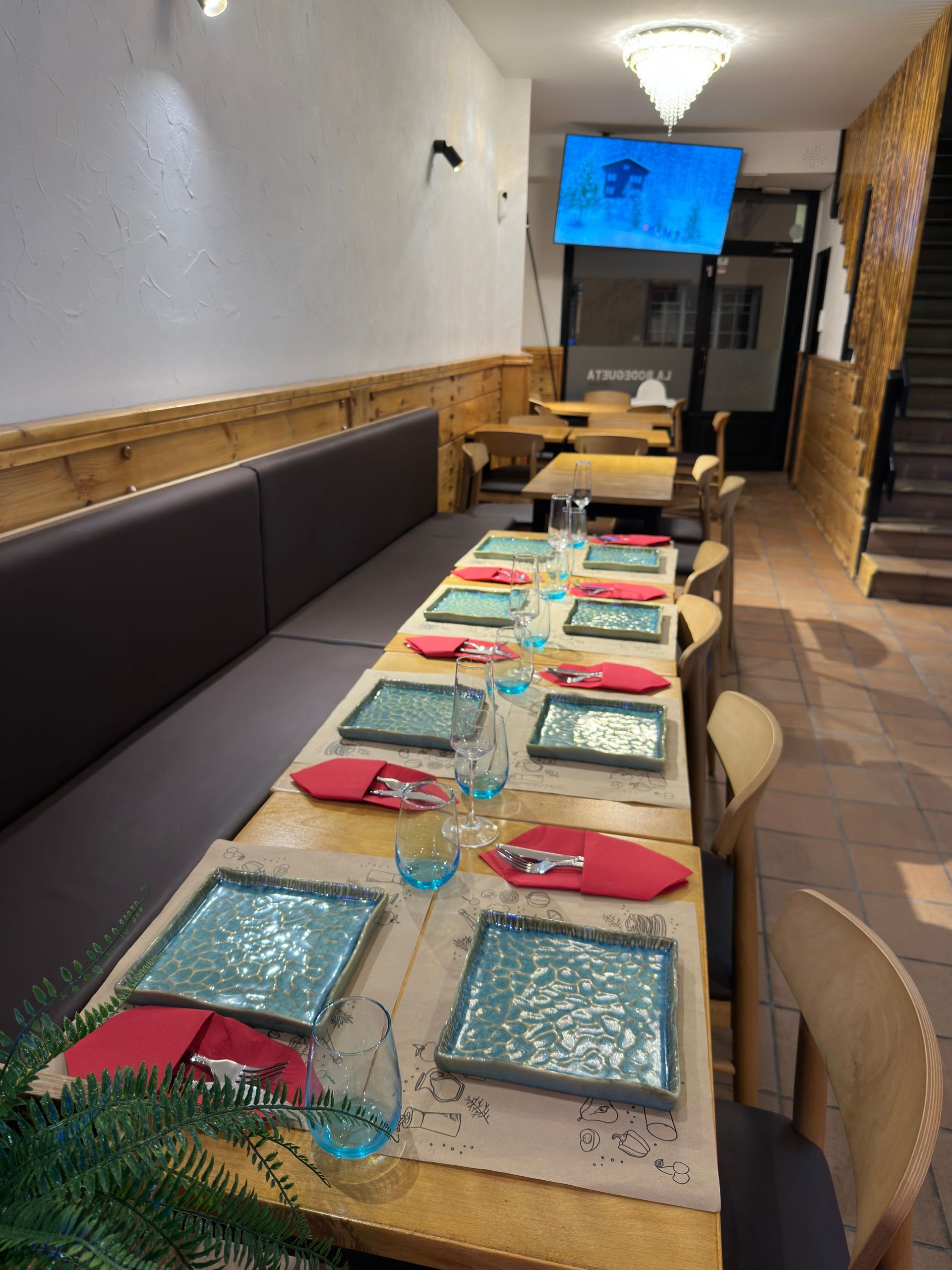 Mesa de comedor larga para invitados en un restaurante con platos cuadrados de color azul verdoso.