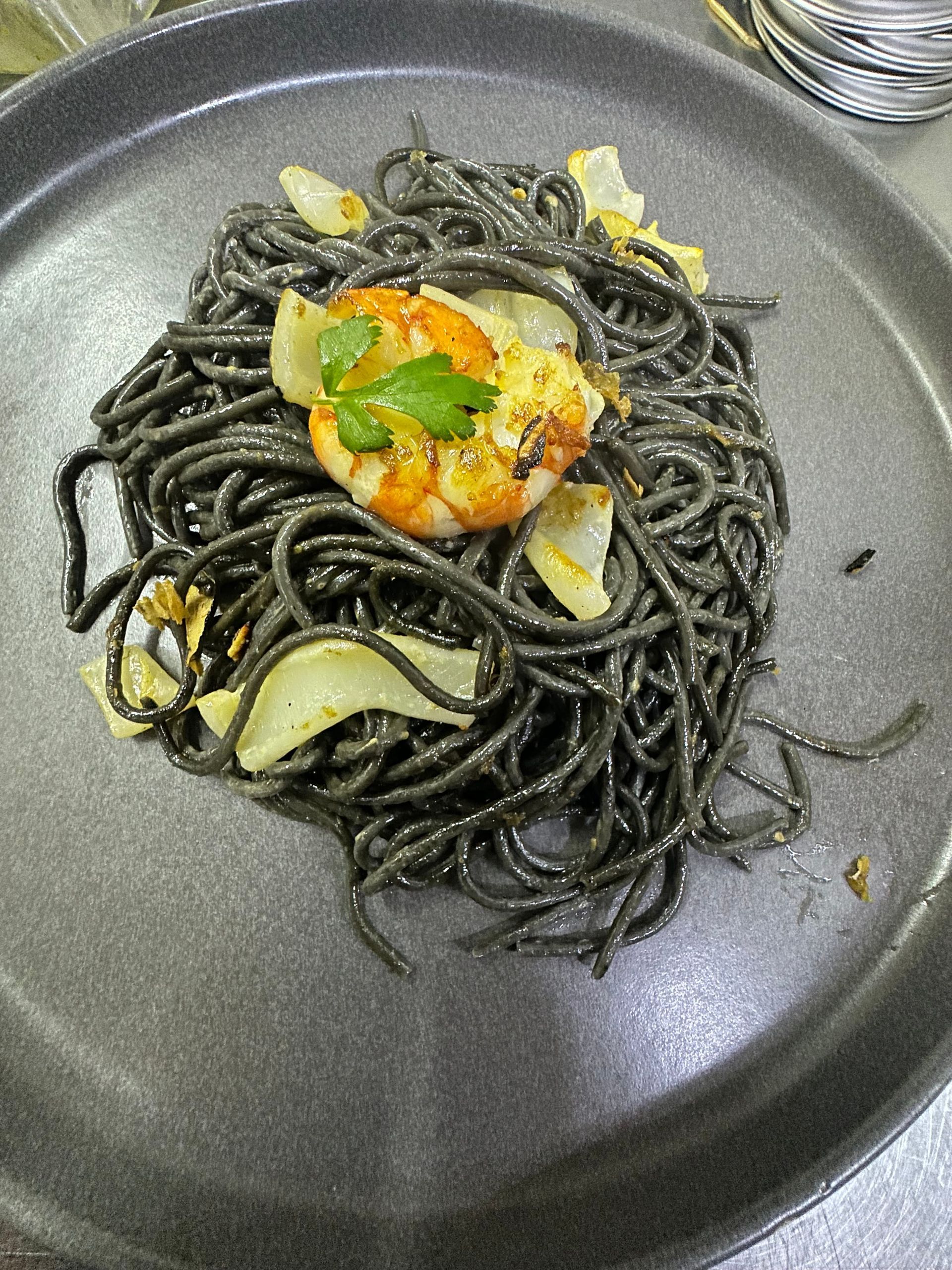Pasta negra con camarones y ajo sobre un plato gris oscuro.