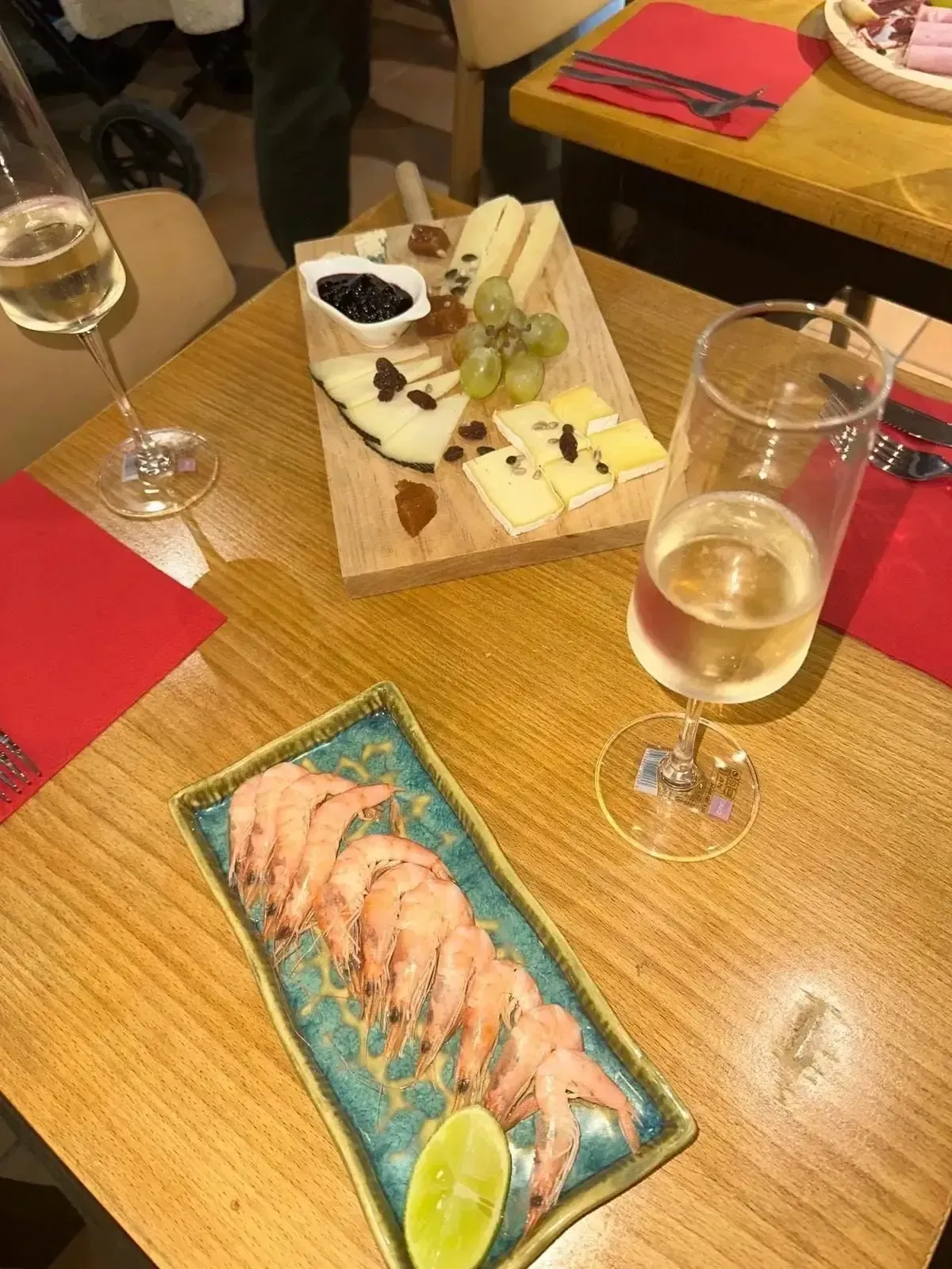 Tabla de quesos, plato de camarones, dos copas de vino blanco, sobre una mesa de madera.