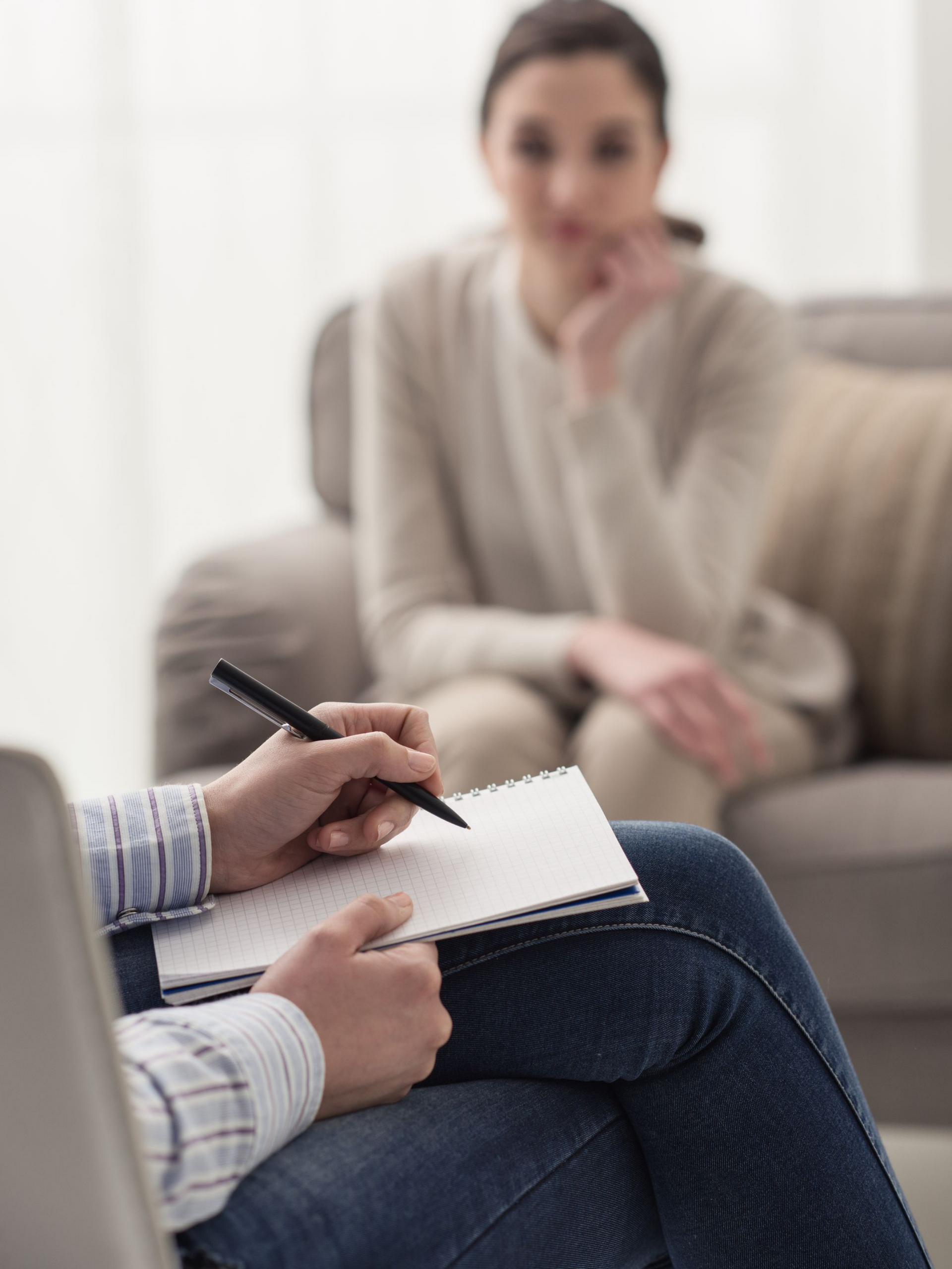 Une personne assise sur une chaise écrite dans un bloc-notes tandis qu'une autre personne est assise en arrière-plan.