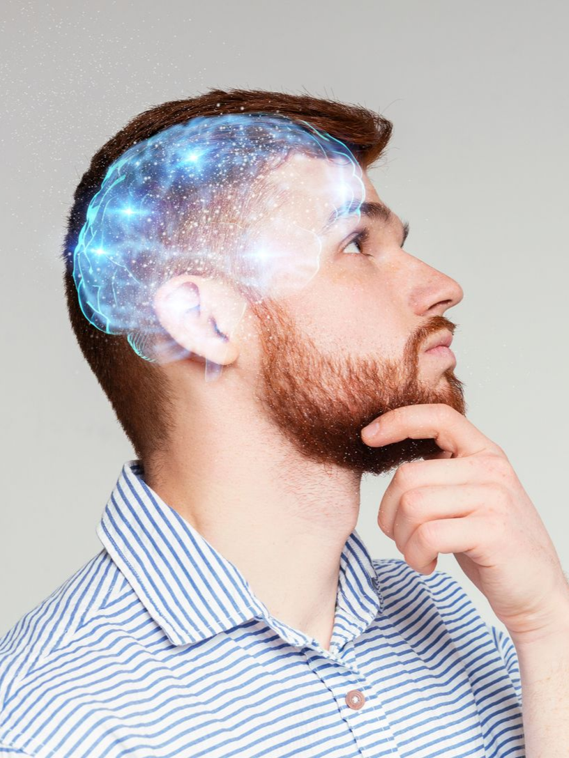Un homme barbu lève les yeux, pensif, un graphique numérique lumineux représentant un cerveau superposé à sa tête.