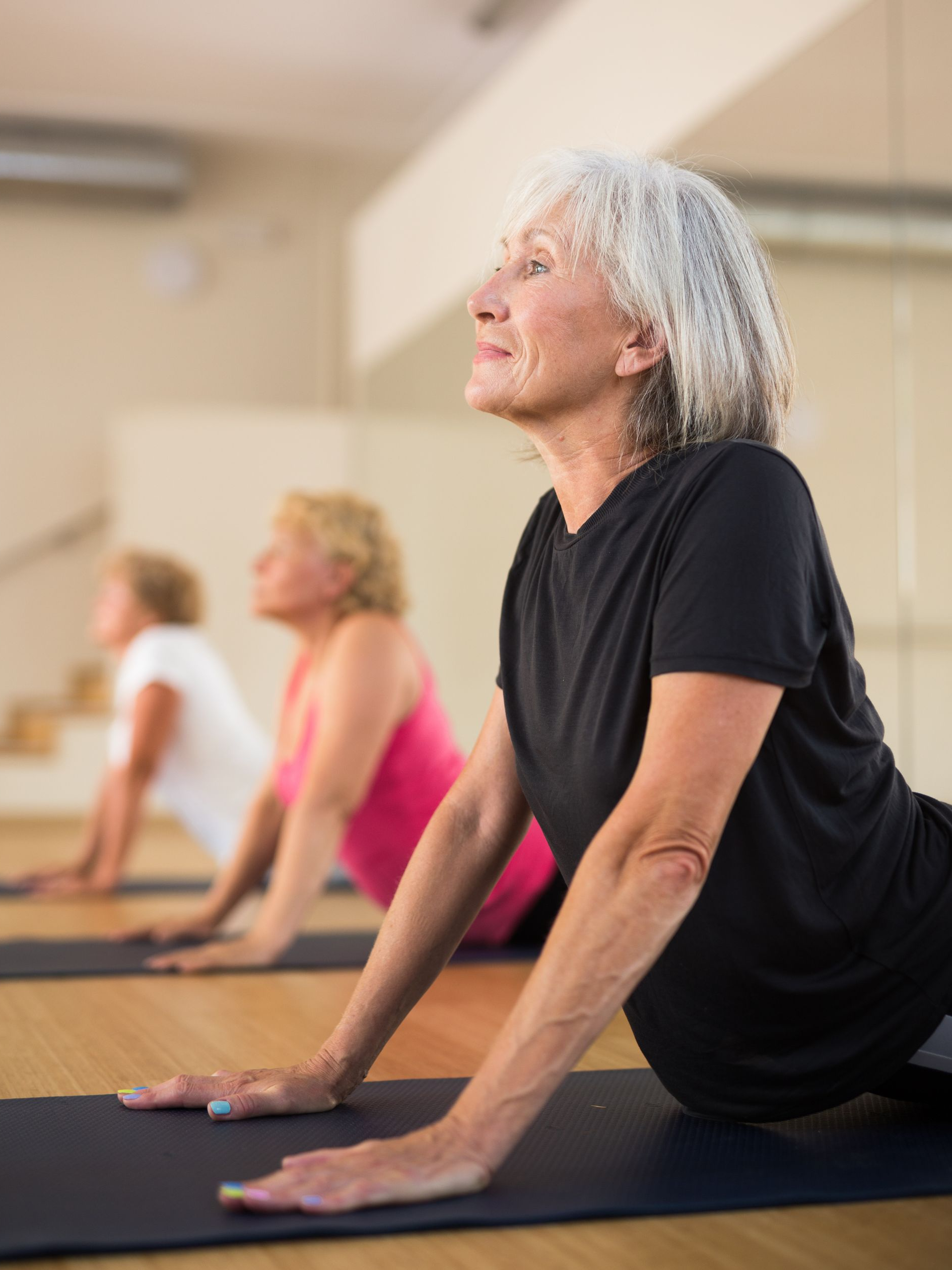 Trois personnes réalisent une posture de yoga face au ciel sur des tapis de sol dans un studio.