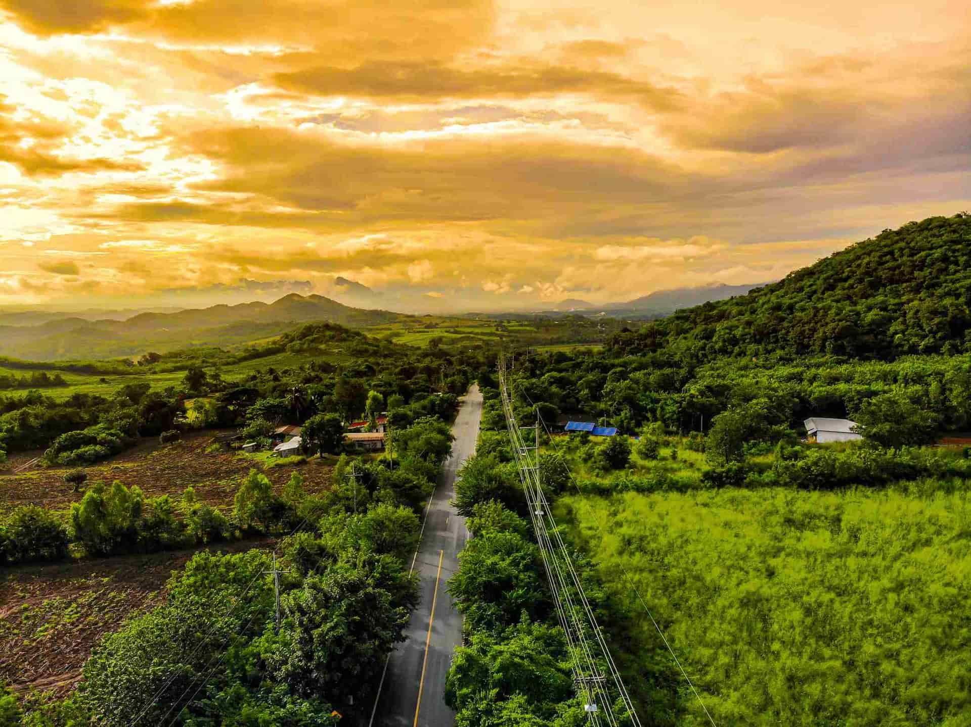 Road through lush green valley under a golden, cloudy sky.