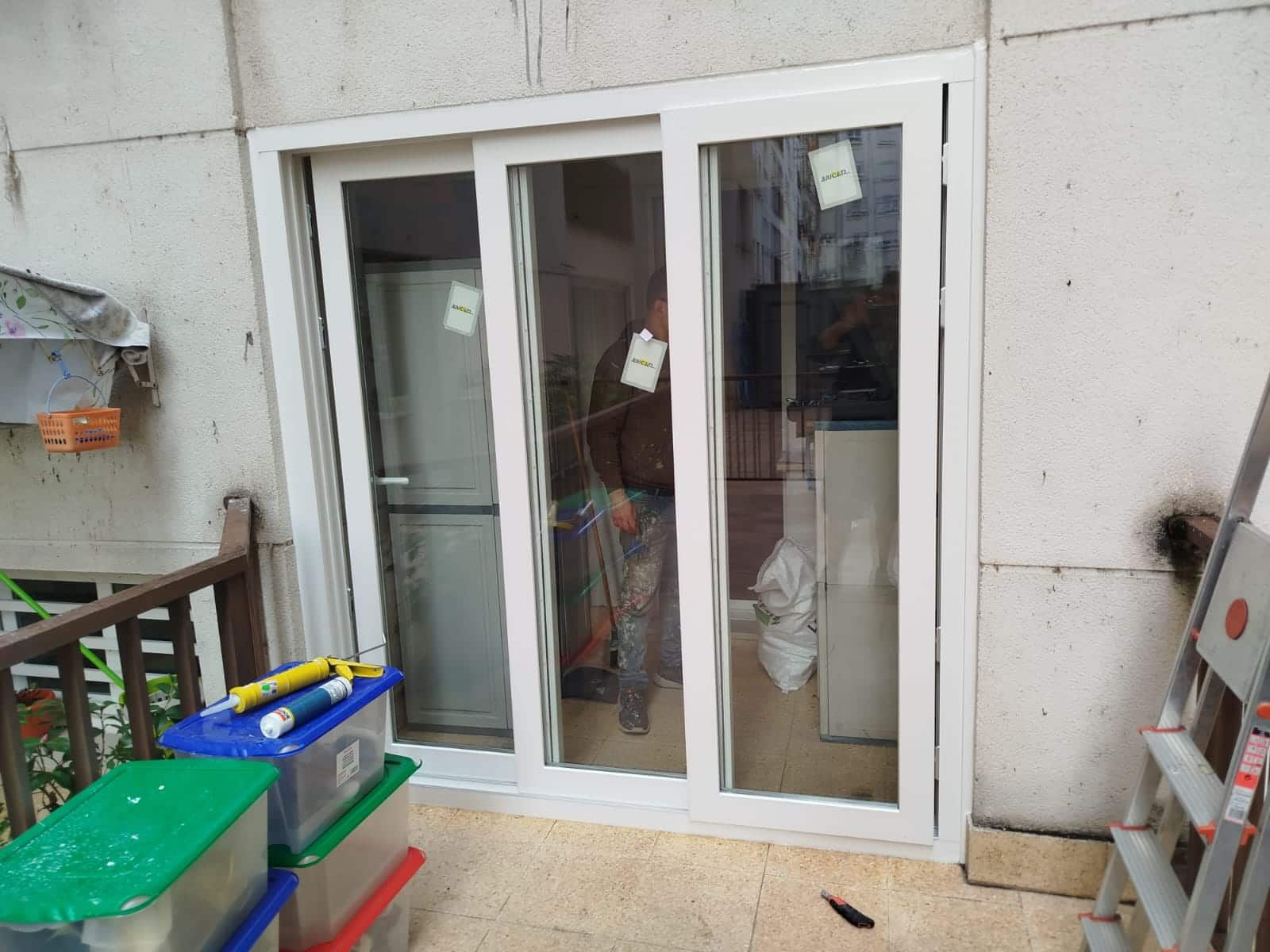 Puerta corrediza de vidrio blanca en un balcón, con herramientas y contenedores en primer plano.