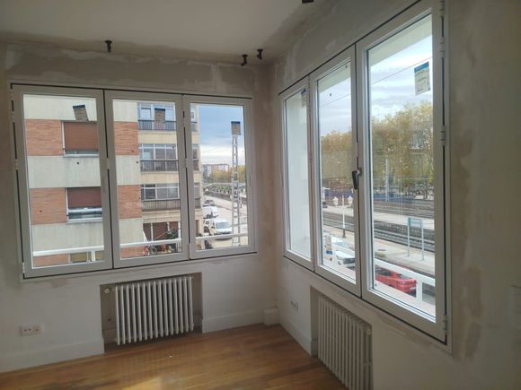 Habitación interior con ventanas y radiadores blancos nuevos; paredes sin terminar. Vista a la ciudad.