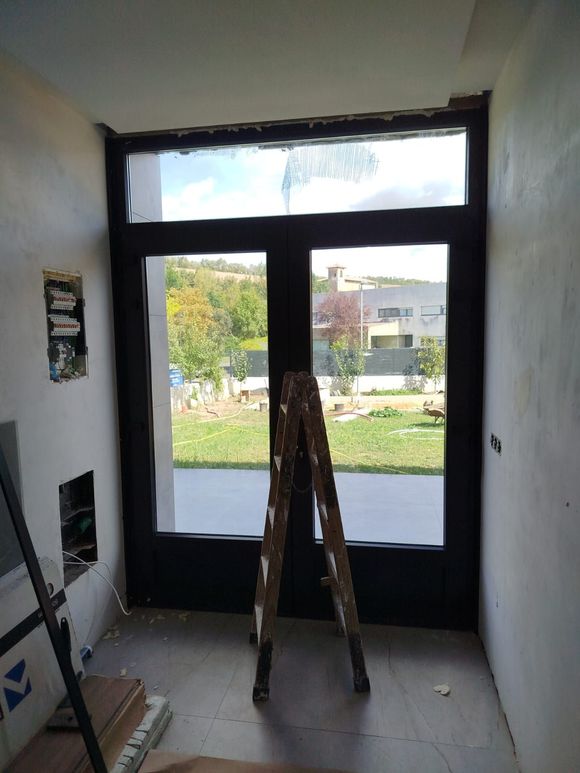 Puerta y ventana de vidrio con marco negro, escalera interior, vista al patio.