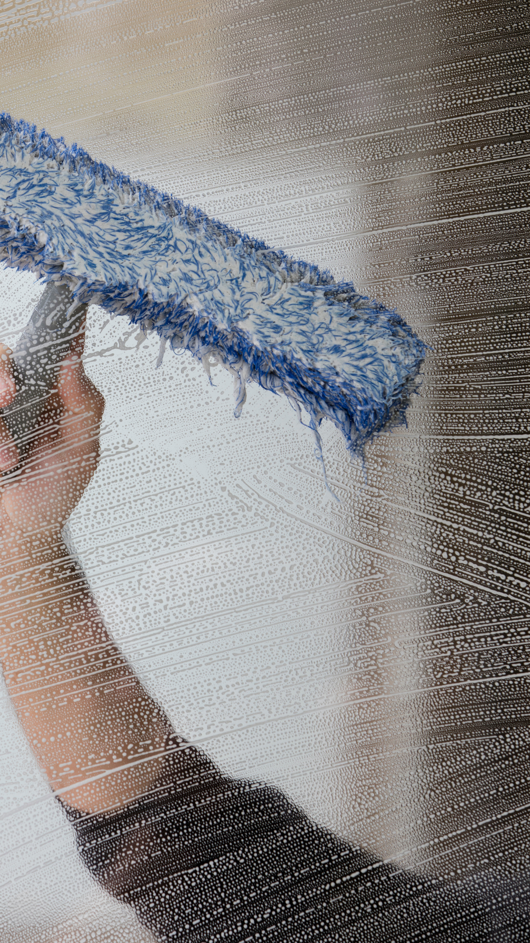 Personne nettoyant une fenêtre avec une serpillière bleue et blanche.