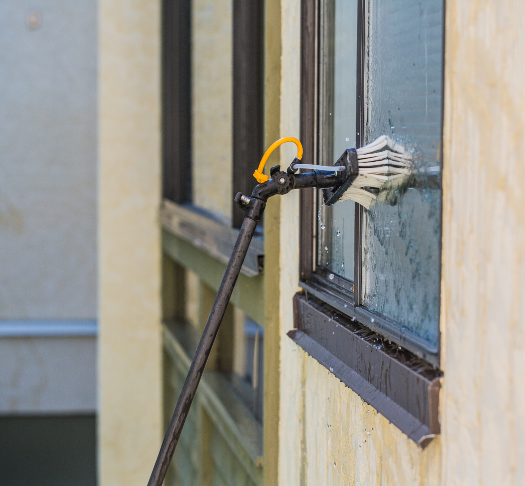 Poteau noir avec une tête de nettoyage frottant une fenêtre sur un bâtiment de couleur crème.
