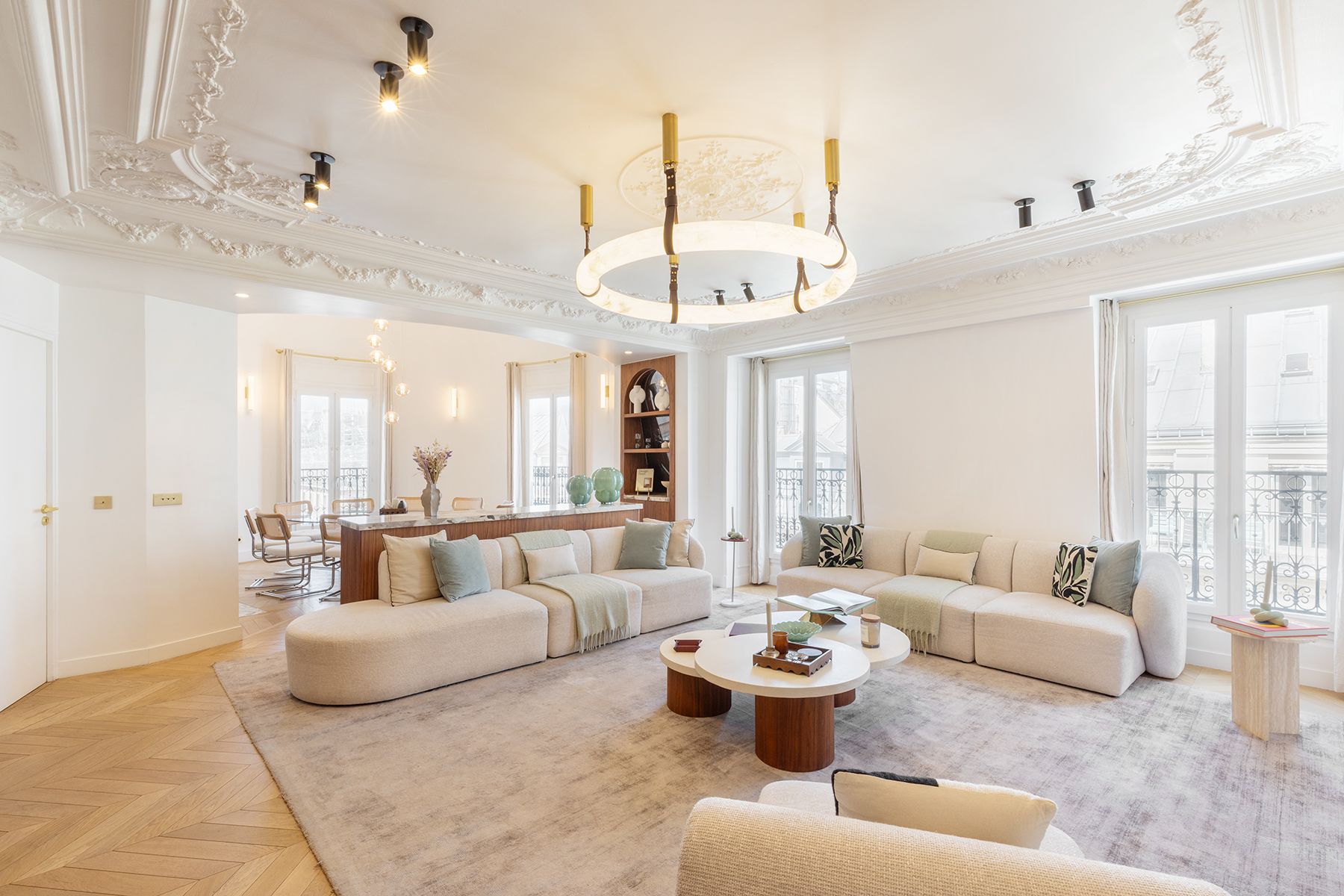 Elegant living room with beige sofas, gold chandelier, large windows, and a glass coffee table