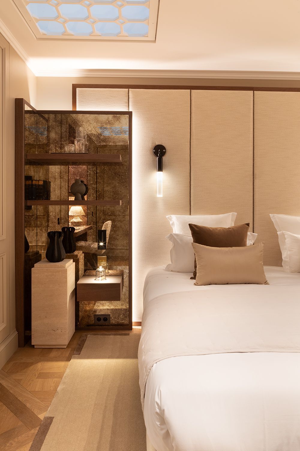 Modern bedroom with a neatly made bed, beige walls, and a built-in shelf with decor and a lamp
