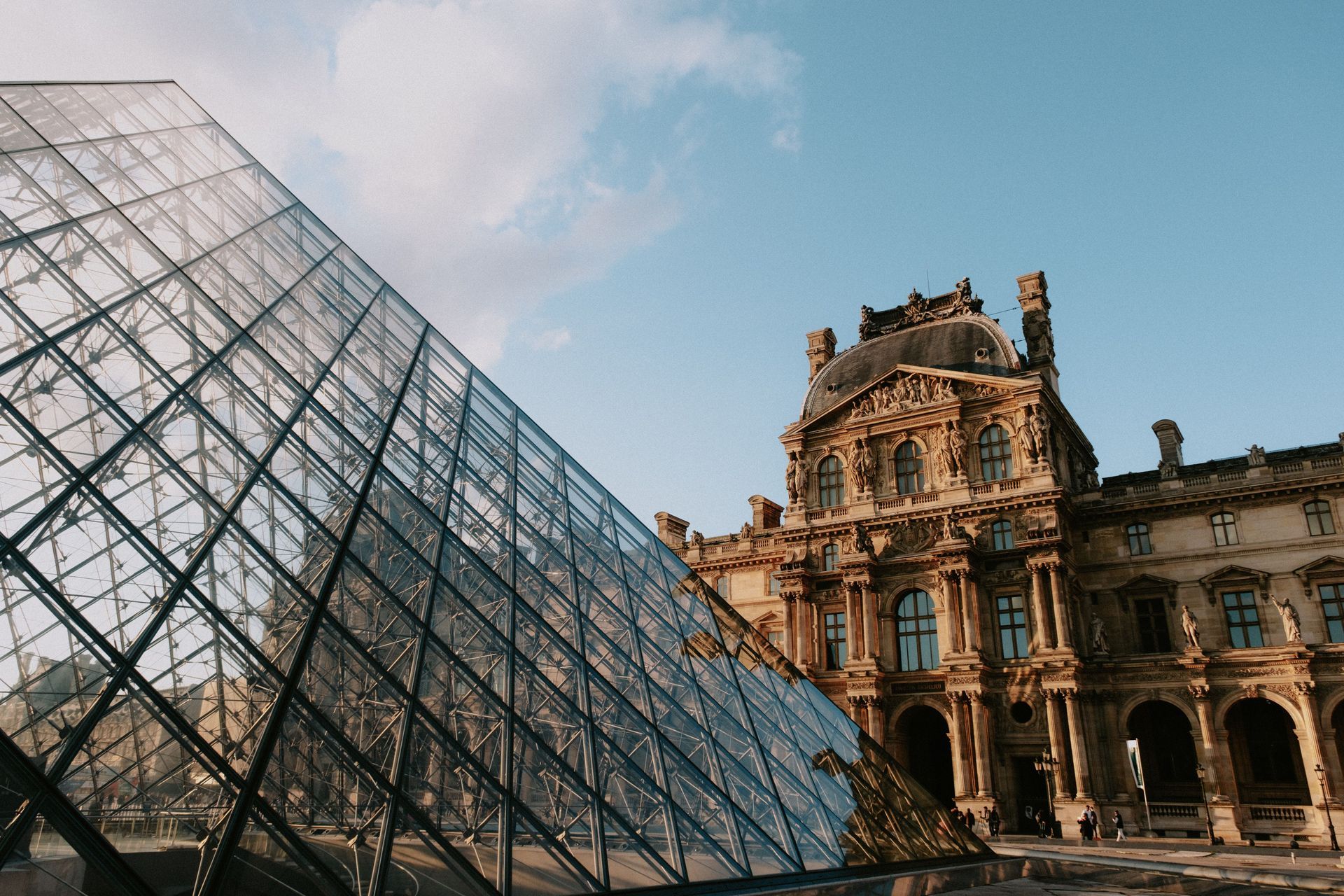 Louvre Museum glass pyramid beside ornate historic façade under a blue sky
