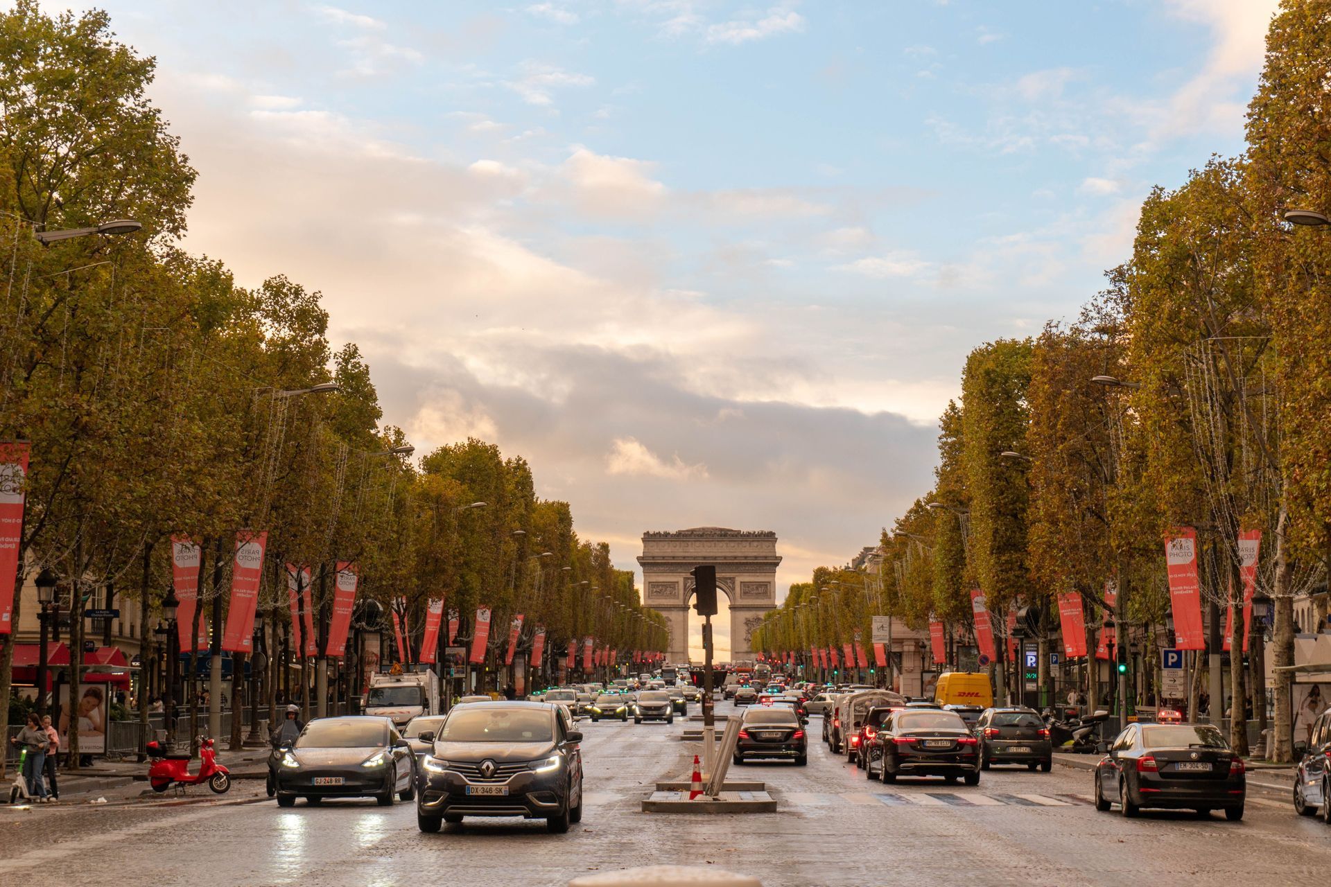 Tree-lined Paris avenue with traffic leading to the Arc de Triomphe at sunset