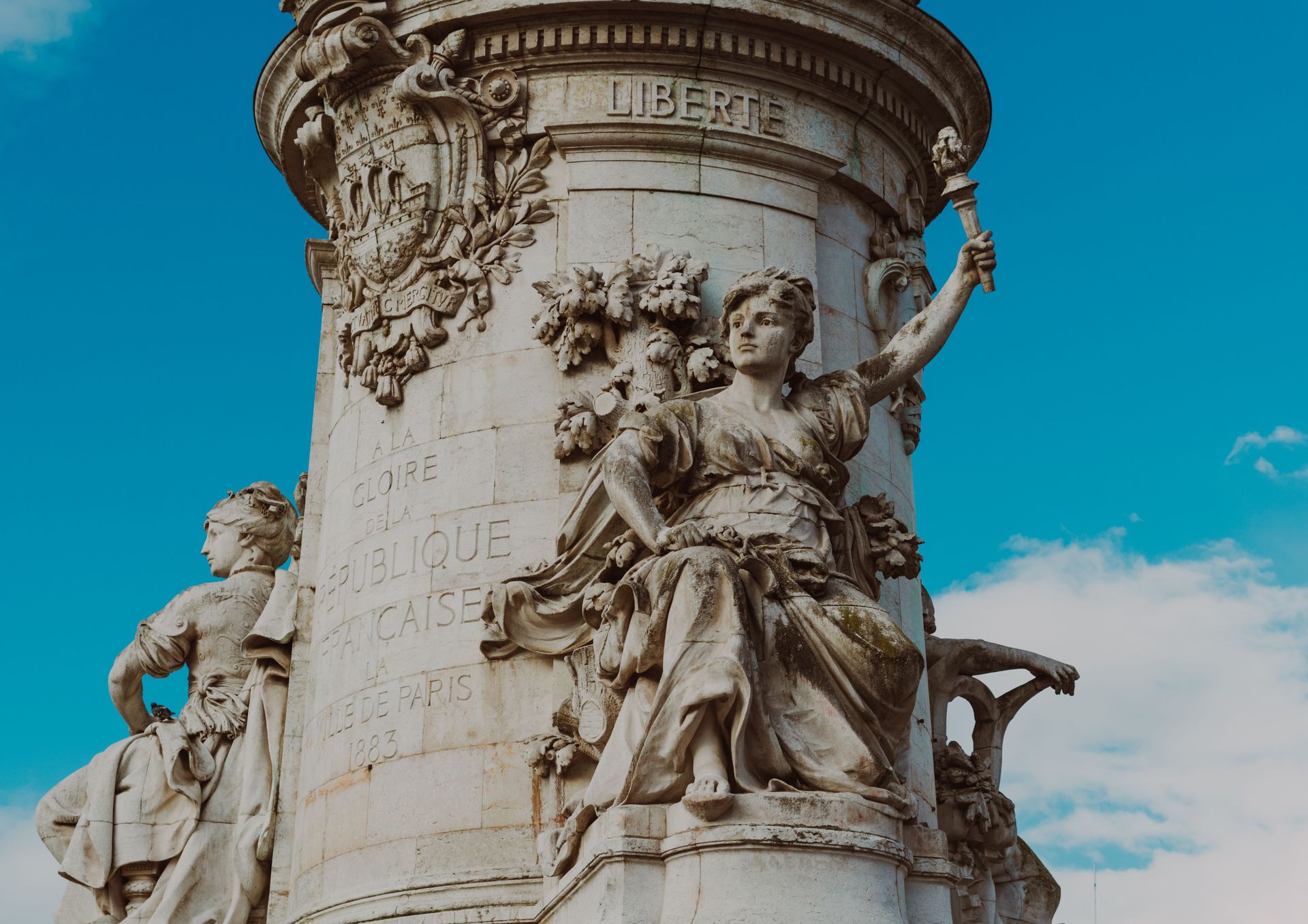 Stone monument with carved classical figures against a bright blue sky