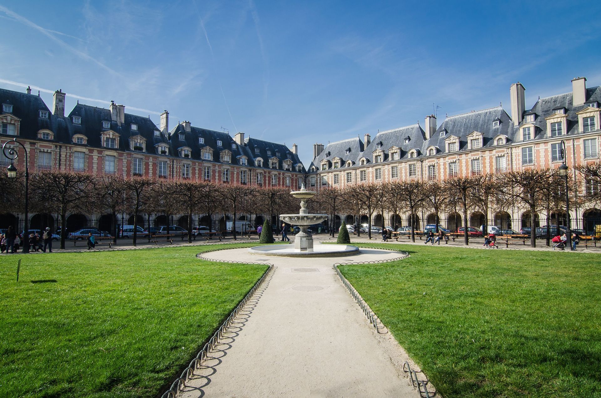 Courtyard with manicured lawns, central fountain, and historic brick buildings under a blue sky